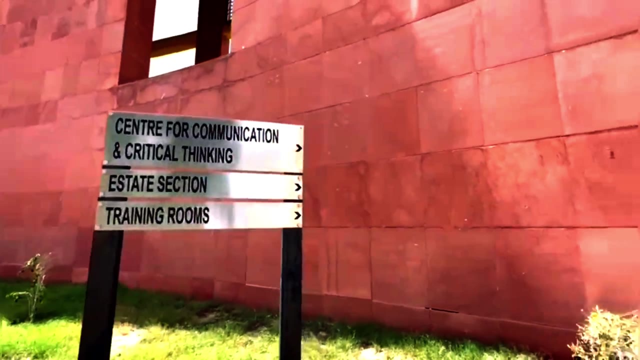 A frame from the film: signposts for the Centre for Communication & Critical Thinking against a red stone wall